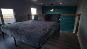 Une chambre à coucher avec un lit, une fenêtre, un ventilateur de plafond et une vue sur l’extérieur.