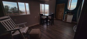Een kamer met een eettafel en stoelen, een raam met uitzicht op een stadsbeeld en een deur naar een andere kamer.