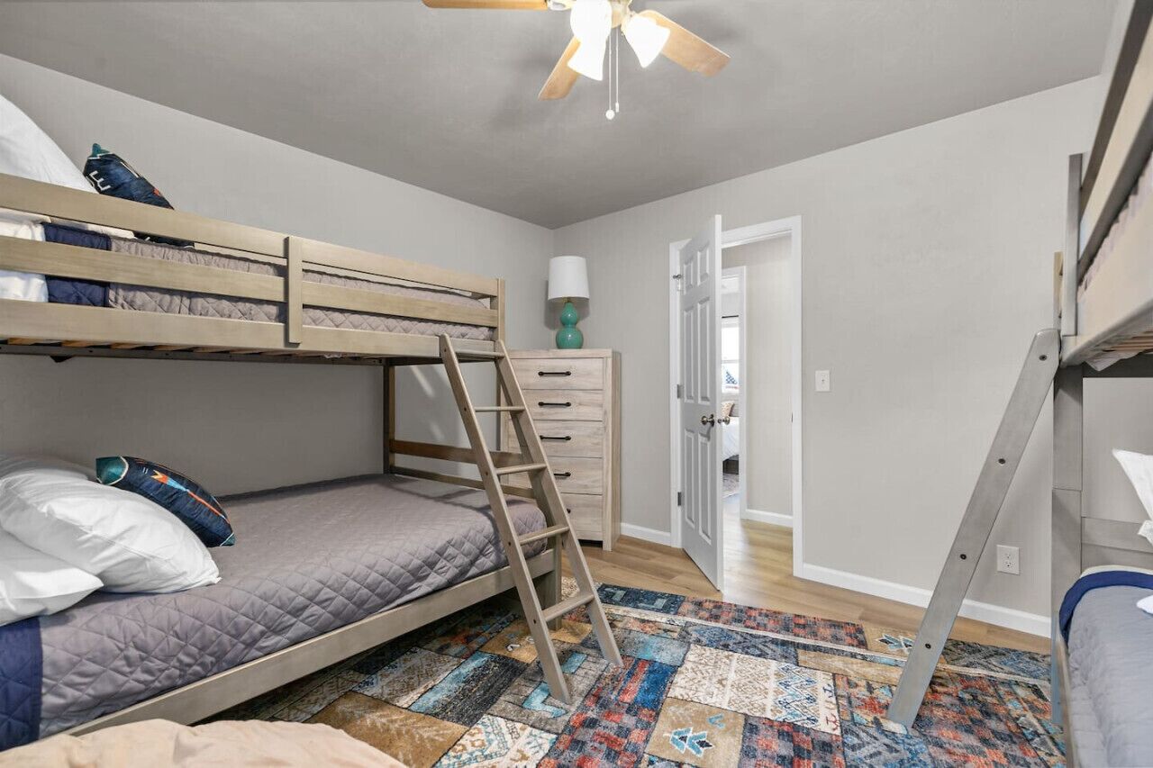 A bunk bed room with a ladder, a dresser, and a patterned rug.