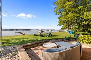 Un patio con mobiliario exterior, vista a un lago y barcos al fondo.