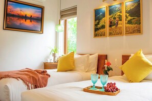 Une chambre d’hôtel avec un grand lit, deux oreillers, une table de chevet avec un vase et une bougie, et des œuvres d’art murales.