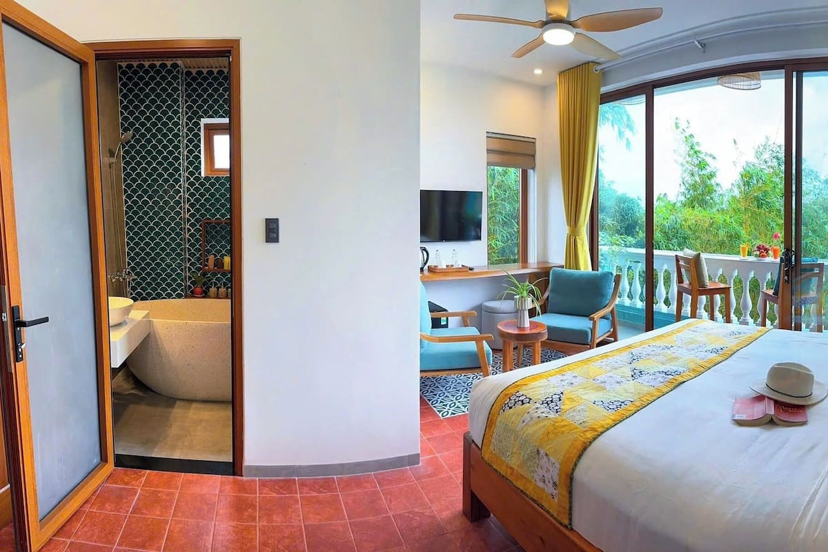 A hotel room with a bed, a seating area with chairs, a balcony with a table, and a TV.