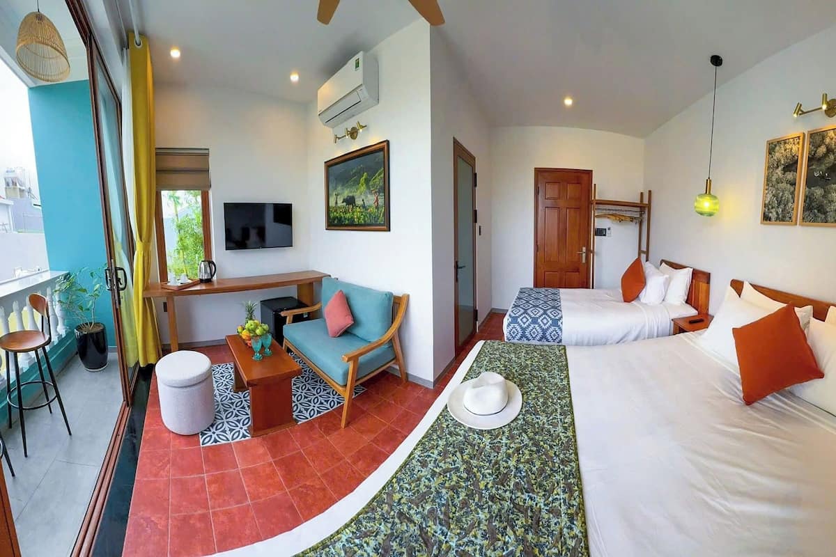 A hotel room with two beds, a TV, a dining area, and a balcony.