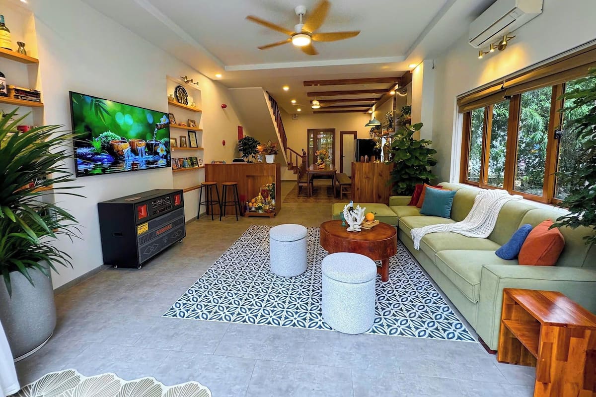 A spacious living room with a large flat-screen TV, a ceiling fan, and a staircase leading to an upper level.
