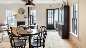 A dining area with a round table, chairs, a fireplace, and a large window. - Charming Cottage in Historic German Village (Columbus)