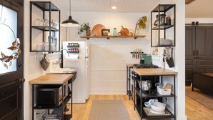 A compact kitchen with wooden countertops, a built-in oven, and a sink. There are shelves above the counter holding various kitchen items and a hanging light fixture. - Charming Cottage in Historic German Village (Columbus)