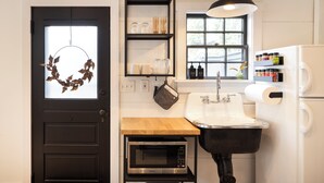 A compact kitchen with a black door, a wooden countertop, a built-in oven, a sink, a hanging light fixture, and a window with a view. - Charming Cottage in Historic German Village (Columbus)