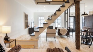 A spacious living area with a wooden floor, a staircase, a sofa, a dining table with chairs, and a fireplace. - Charming Cottage in Historic German Village (Columbus)