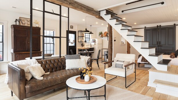 A spacious living area with a brown leather sofa, a round coffee table, and a staircase leading to a second floor. - Charming Cottage in Historic German Village (Columbus)