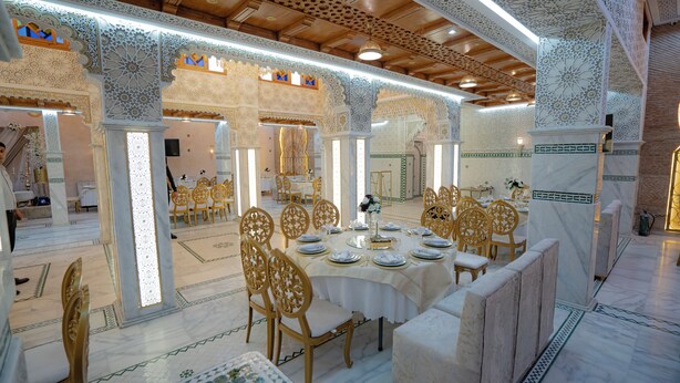 A luxurious dining area with ornate white and gold decor, marble flooring, and a long table set for a meal. - Riad Golden Mansour  (Meknes)