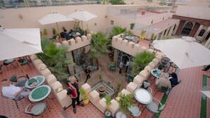 An outdoor café with tables and chairs, surrounded by potted plants and umbrellas. - Riad Golden Mansour  (Meknes)