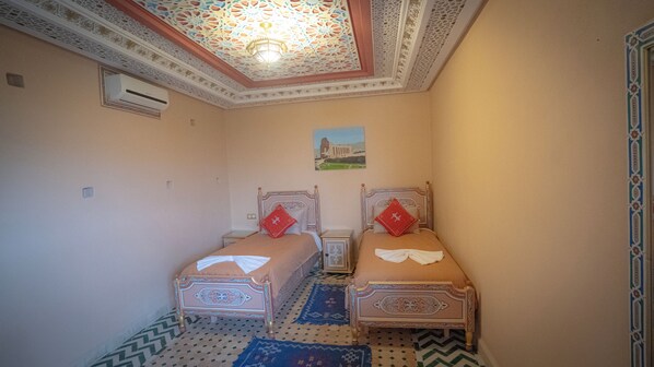 Een kleine, klassieke kamer met twee bedden, kamerbreed tapijt met patroon en een decoratief plafond.