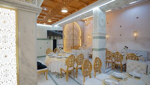 A dining area with ornate white and green patterned walls, a high ceiling with intricate woodwork, and a central decorative light fixture. - Riad Golden Mansour  (Meknes)