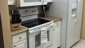 Una cocina con armarios blancos, un microondas, un refrigerador, un horno y un bloque de cuchillos.