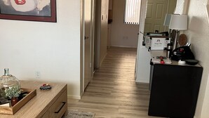 Un pasillo con suelo de madera, un escritorio con cajones, un jarrón con una planta y un cuadro en la pared.
