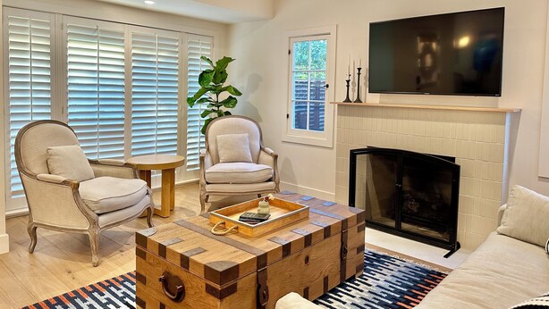 Un salon avec une cheminée, deux fauteuils, une table basse et un téléviseur fixé au-dessus de la cheminée.
