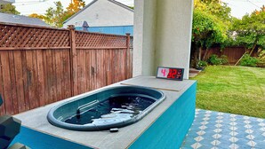 Un bain à remous doté d’une horloge numérique, entouré d’une clôture en bois et d’une terrasse carrelée.