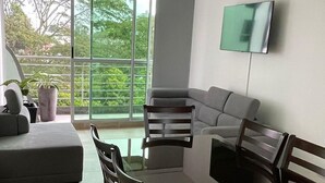 Uma sala de estar moderna com uma mesa de jantar, cadeiras, um sofá e uma televisão presa à parede.