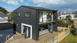 A modern two-story house with a balcony, large windows, and a wooden deck. - Modern Bach (Waihi Beach)