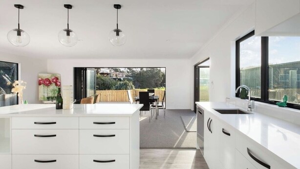 A modern kitchen with white cabinetry, a central island, and pendant lighting. - Modern Bach (Waihi Beach)