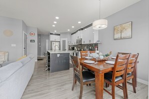 A modern kitchen with white cabinets, a central island, and a dining area with wooden chairs and a table set for two. - Luxury in Laurel-8 guests+1 Baby,4 beds,2.5 bath,1 car Grg,
offer w direct book. (Edmonton)