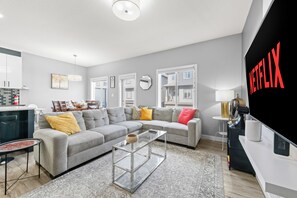 A modern living room with a grey sectional sofa, a glass coffee table, and a flat-screen TV mounted on the wall. - Luxury in Laurel-8 guests+1 Baby,4 beds,2.5 bath,1 car Grg,
offer w direct book. (Edmonton)
