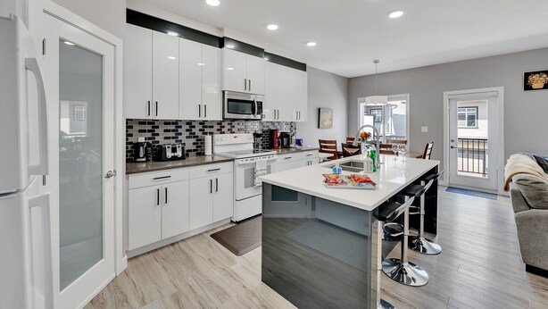 A modern kitchen with white cabinets, a central island, and a dining area with a sofa and chairs. - Luxury in Laurel-8 guests+1 Baby,4 beds,2.5 bath,Dbl Grg,discount w direct book. (Edmonton)