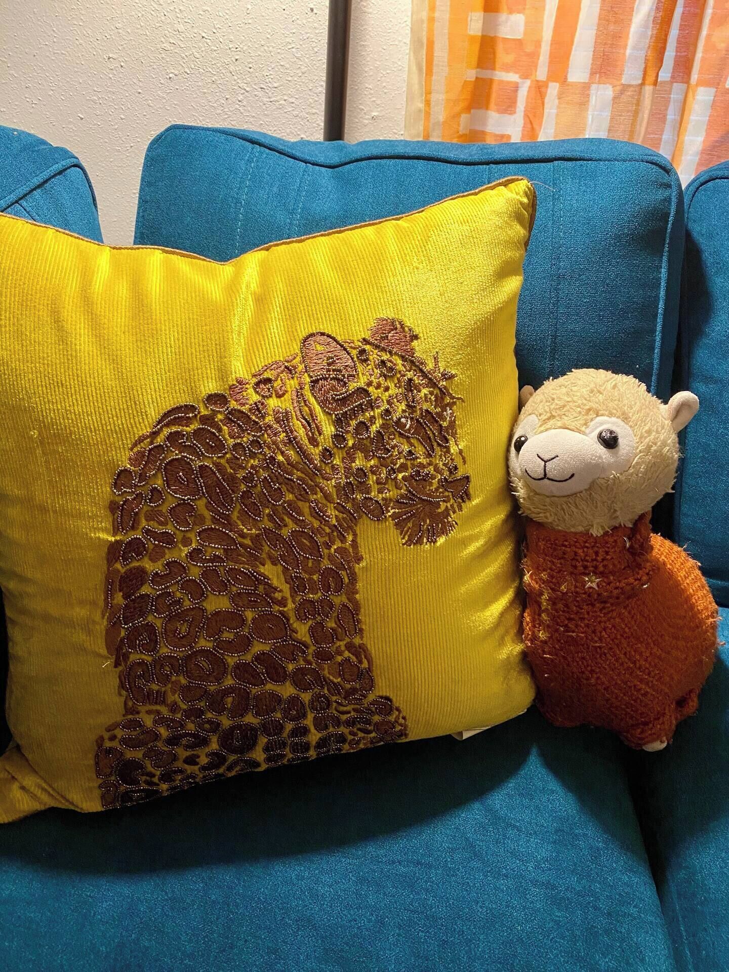 Ein blaues Sofa mit einem gelben Kissen, das ein Bärenmotiv und ein kleines Stoffschaf zeigt.