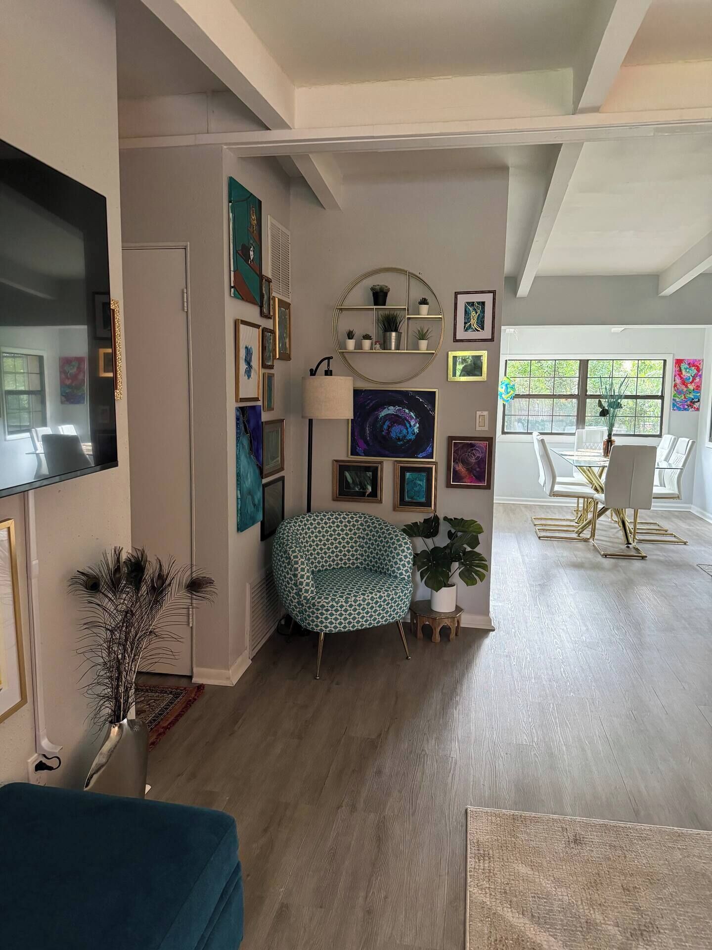 Uma sala de estar ampla com uma TV grande, uma mesa de centro redonda e um espaço de jantar com uma mesa e cadeiras brancas.
