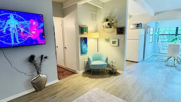 A modern living room with a flat-screen TV, a blue armchair, and a dining area with a table and chairs.