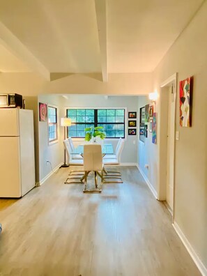 A modern kitchen with white appliances and a dining area with a glass table and chairs. - Nina Juniper Art House Exhibit (Gainesville)