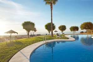 A swimming pool with a curved edge, surrounded by grass and trees, and a fence enclosing the area. - Great Apartment With View (Mijas)