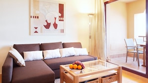Ein modernes Wohnzimmer mit einem braunen Sofa, einem Glastisch mit Obst und einem großen abstrakten Gemälde an der Wand.