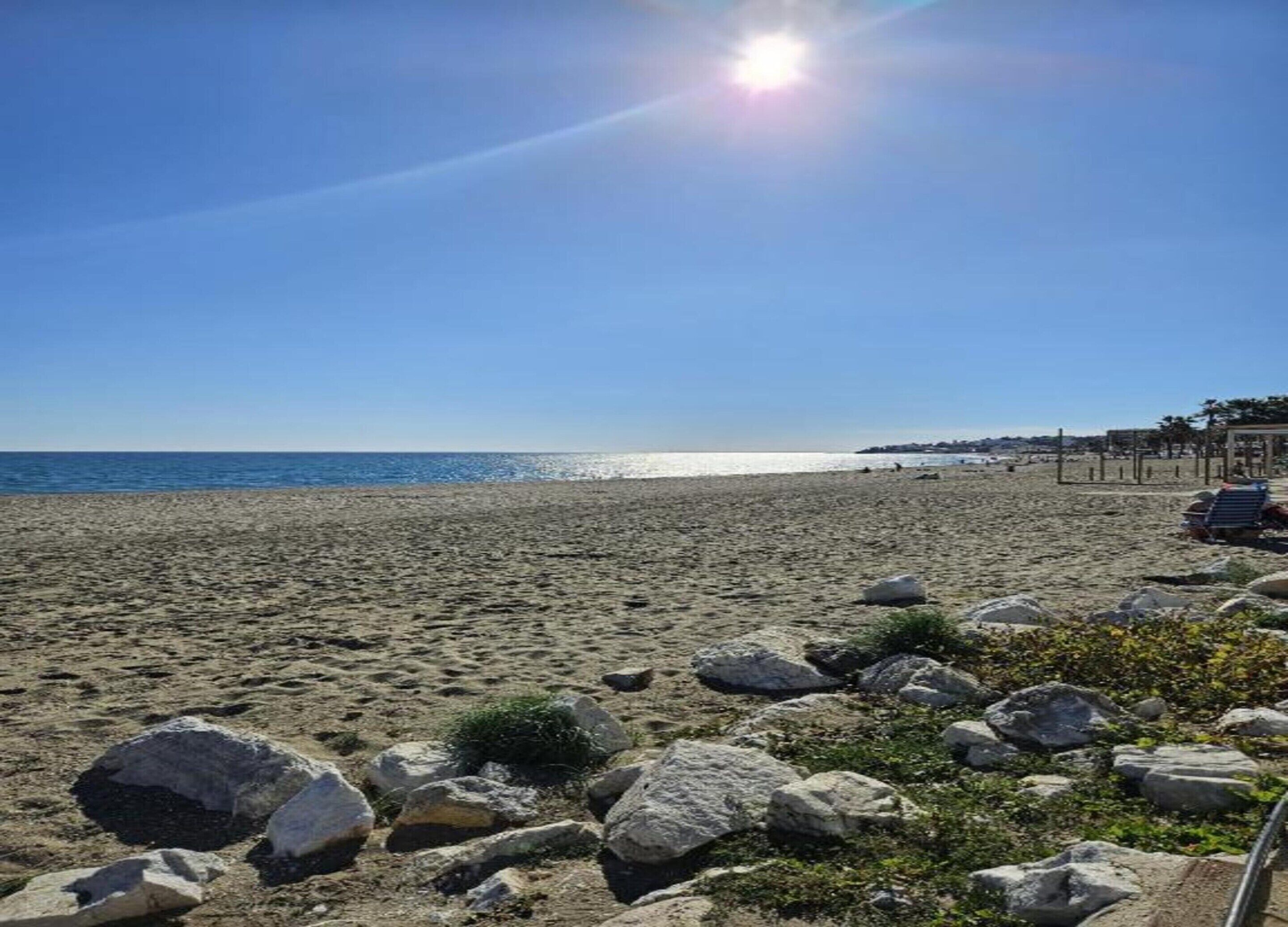 A beach with large rocks in the foreground and a clear view of the ocean.
