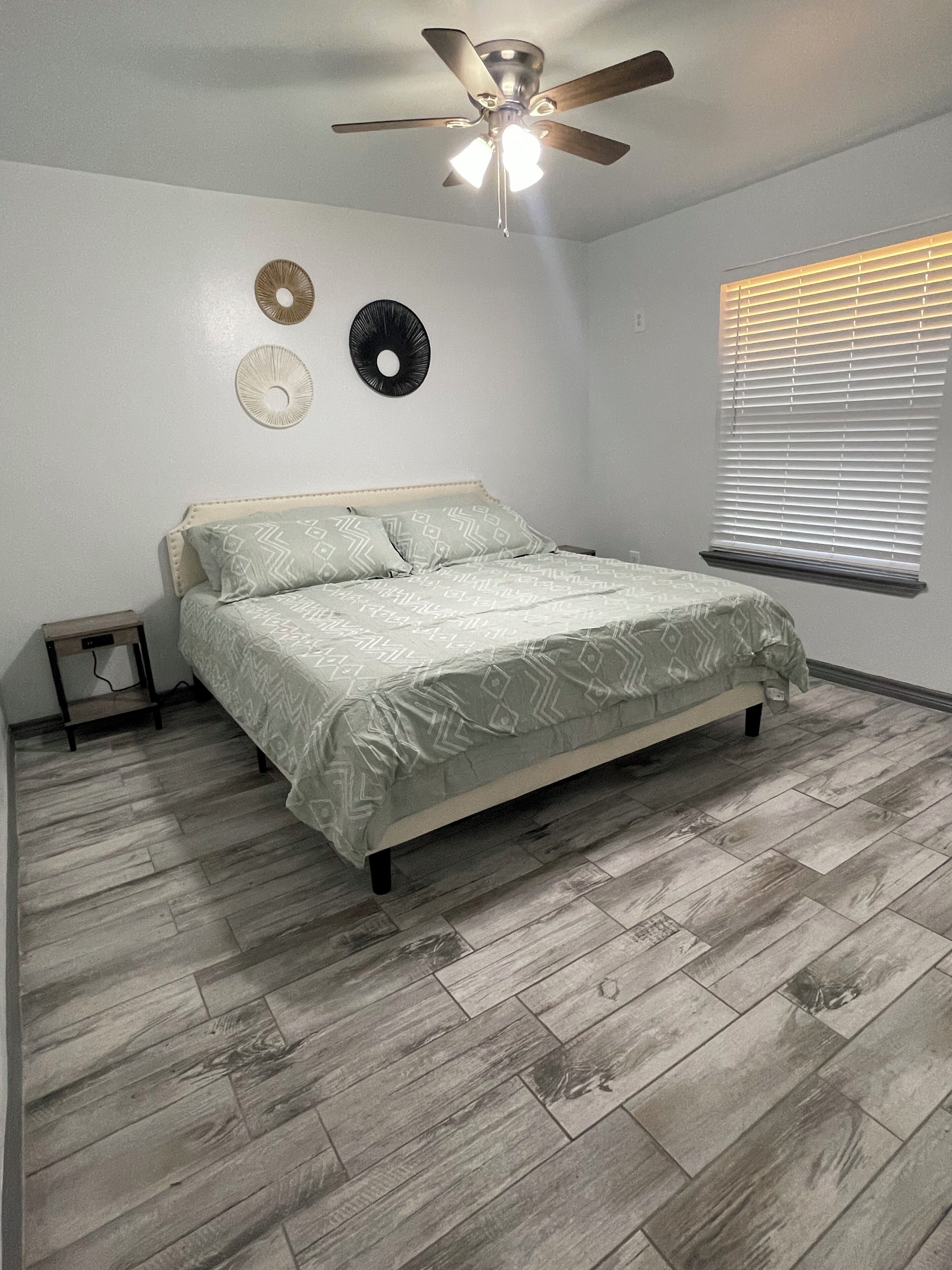 Une chambre à coucher avec un lit, un ventilateur de plafond, une horloge murale et une fenêtre avec des stores.