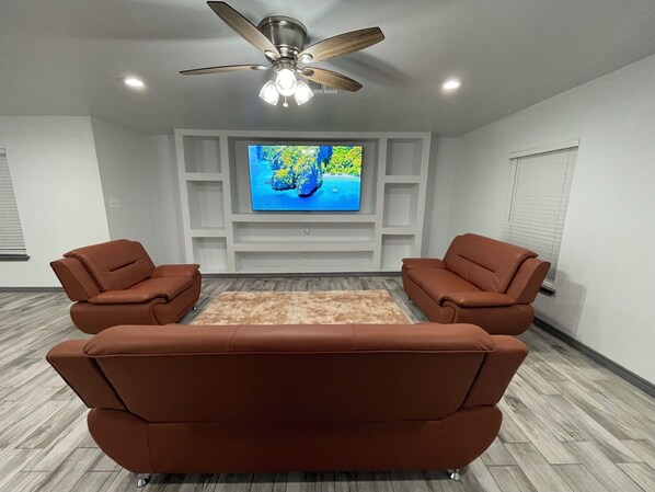 A living room with a flat-screen TV mounted on a white wall, two brown leather sofas, a wooden floor, and a ceiling fan. - Modern 3-bedroom 2-Bathroom home Conveniently located next to Texas Roadhouse!   (Del rio)