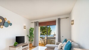 Un salón moderno con una televisión de pantalla plana, una mesa de centro, un sofá y un balcón con vistas al mar.