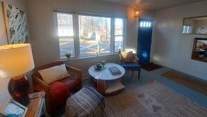 Una sala de estar acogedora con un sofá, una mesita redonda pequeña, una silla y un ventanal con vistas al exterior.