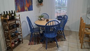 Un comedor con una mesa redonda de madera, sillas azules, una planta colgante y una estantería con botellas de vino.