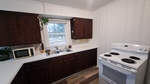 Una cocina con armarios de madera oscura, encimera blanca, microondas, pileta y estufa blanca.