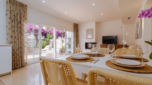 A dining area with a white table set for four, wicker chairs, and a TV in the background. - House in Marbella Near Beaches (Marbella)