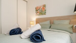 A neatly made bed with rolled towels, a wall-mounted lamp, and a floral painting. - House in Marbella Near Beaches (Marbella)