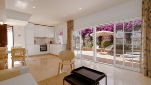 A spacious living area with a kitchen, a dining set, and a large sliding glass door leading to an outdoor patio with a view of purple flowers. - House in Marbella Near Beaches (Marbella)