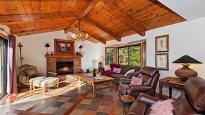 Una sala de estar acogedora con chimenea, sofás de cuero, una mesa de centro de madera y un ventanal con vistas a la vegetación.