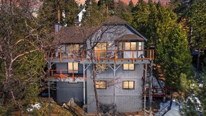 Una casa de dos pisos con balcón y terraza, rodeada de árboles y nieve.