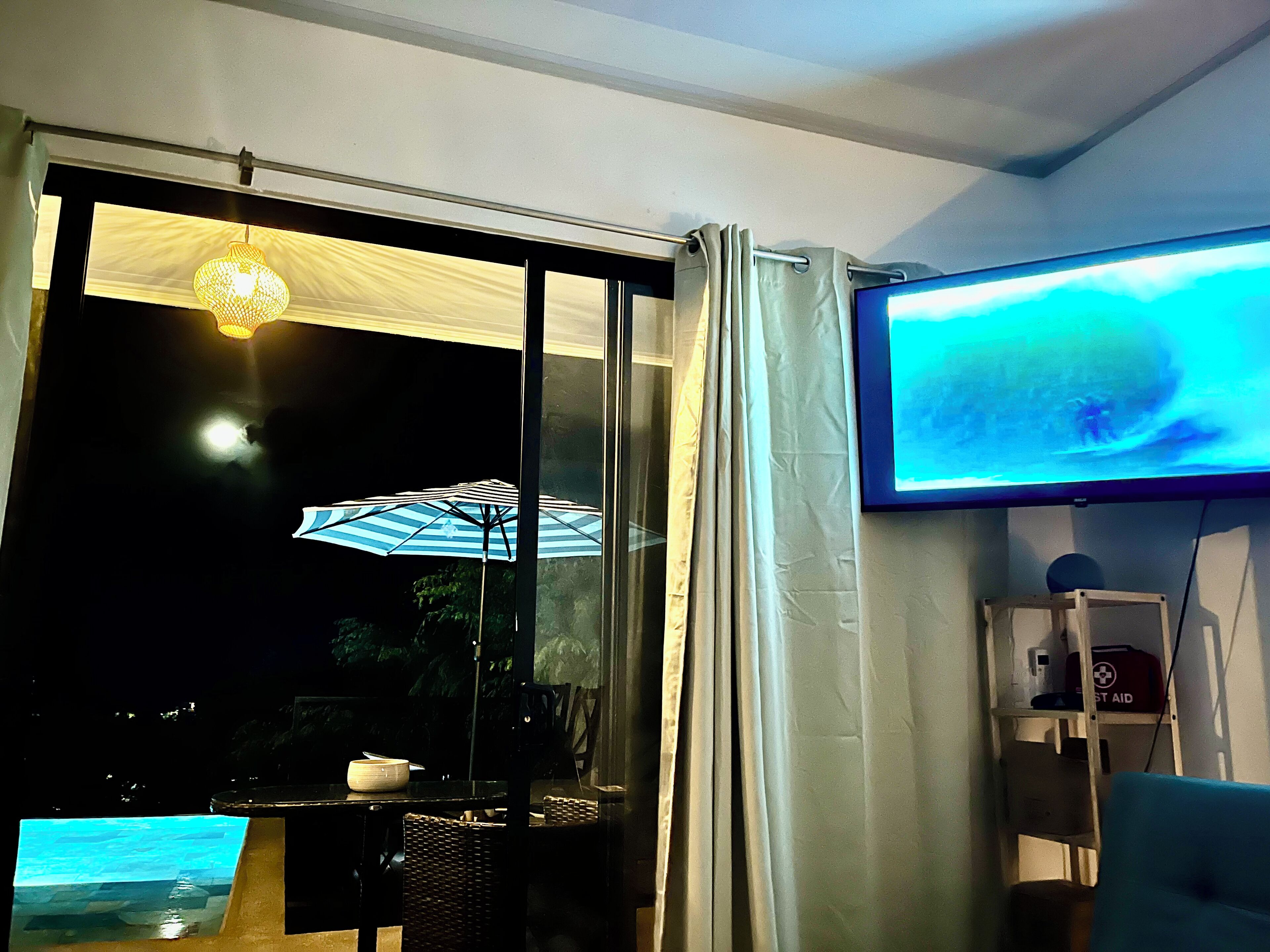 A room with a large window, a television, and a table with an umbrella.