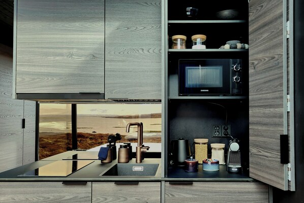 A modern kitchen with a built-in microwave, stainless steel sink, and wooden cabinetry. - Mystic Light Lodge (Budardalur)