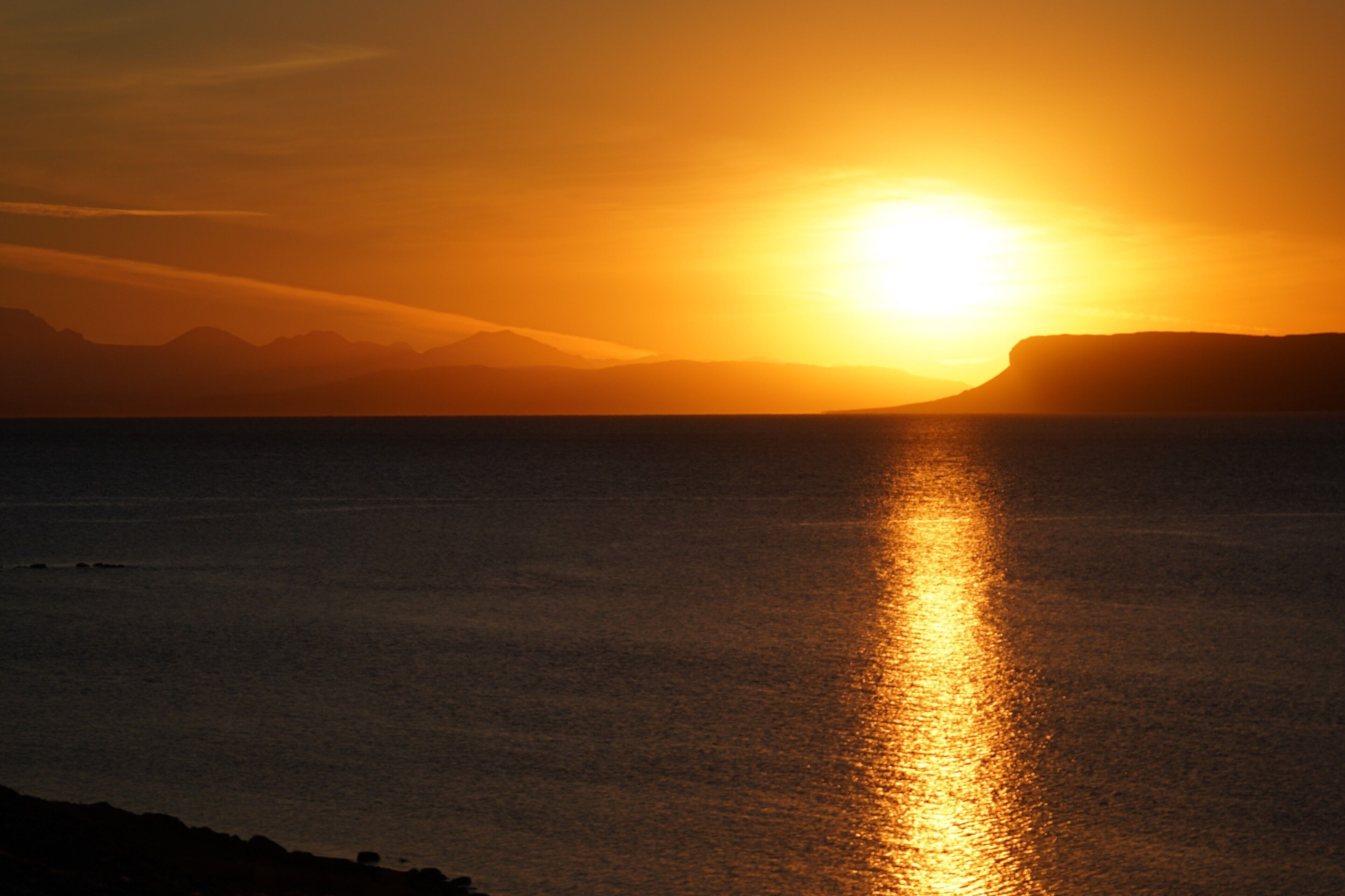 A sunset over a calm sea with distant mountains.