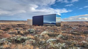 Ein modernes Gebäude mit einer reflektierenden Glasfassade, eingebettet in eine karge Landschaft mit vereinzelter Vegetation.