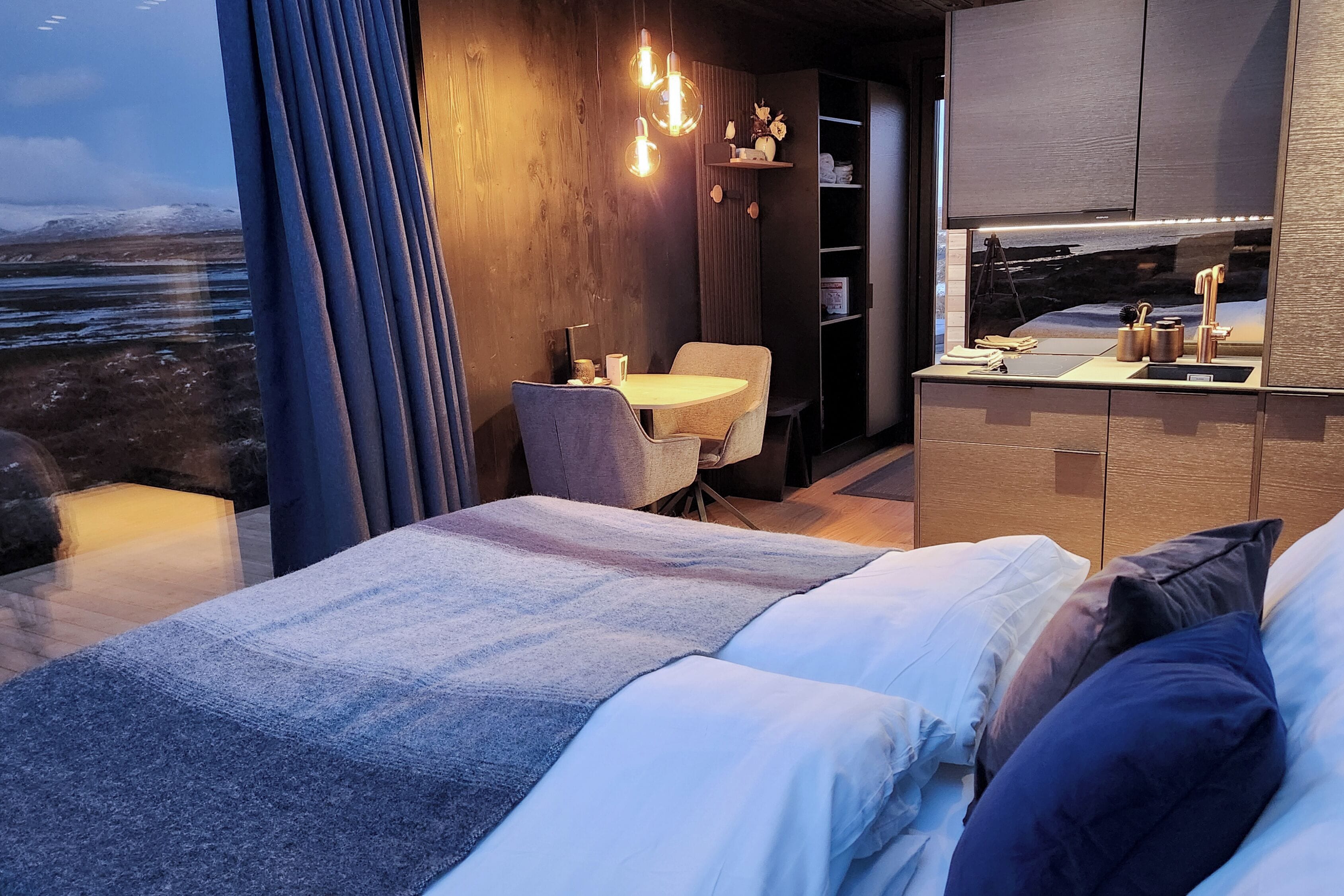 Una camera da letto moderna con un letto, un tavolino e una sedia. Si apre una vista sull'esterno attraverso una finestra.